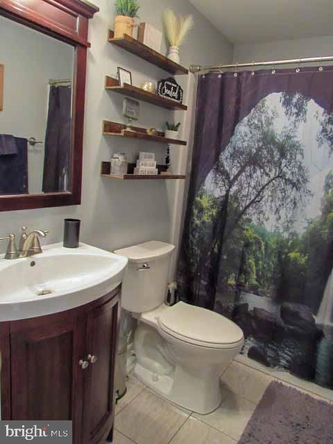 full bath featuring curtained shower, toilet, vanity, and tile patterned flooring