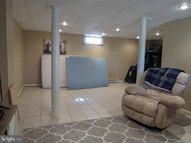 basement featuring light tile patterned floors, a paneled ceiling, baseboards, and baseboard heating