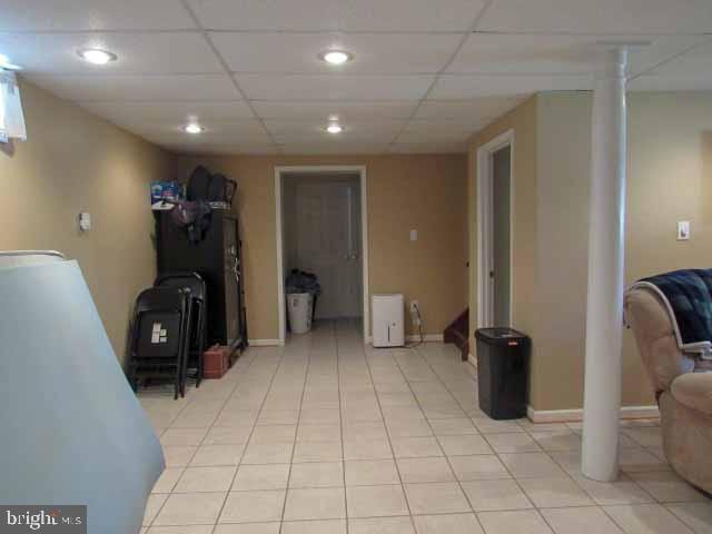 finished below grade area featuring light tile patterned floors, a drop ceiling, and baseboards