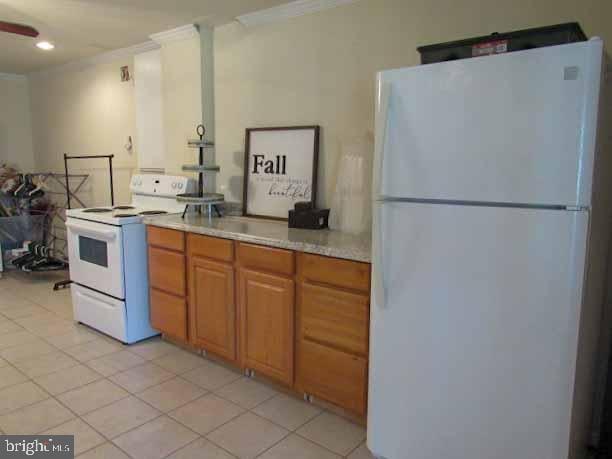 kitchen with crown molding, light countertops, light tile patterned floors, brown cabinets, and white appliances