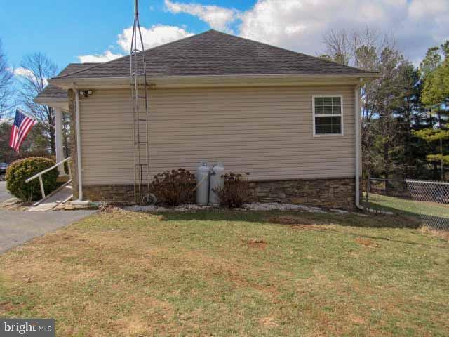 view of side of home featuring a lawn, roof with shingles, and fence