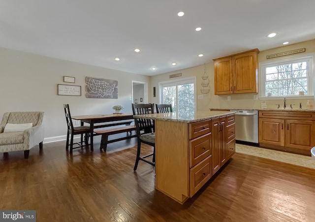 kitchen with dishwasher, dark wood-style flooring, a sink, and a kitchen breakfast bar