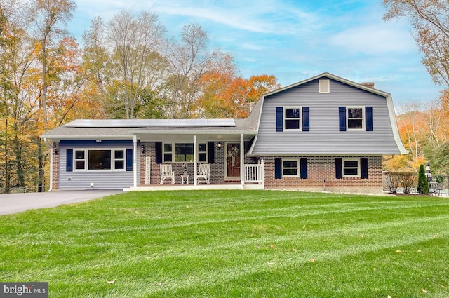 split level home with brick siding, solar panels, a gambrel roof, covered porch, and a front yard