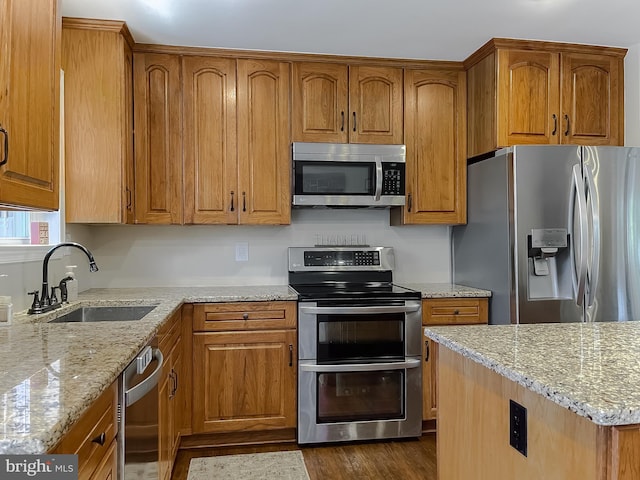 kitchen featuring stainless steel appliances, dark wood-style flooring, a sink, light stone countertops, and brown cabinetry