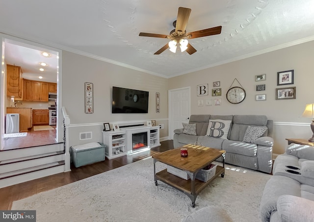 living area with ceiling fan, visible vents, wood finished floors, and ornamental molding