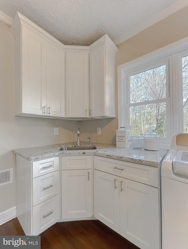 kitchen with white cabinets, light stone counters, dark wood-type flooring, separate washer and dryer, and a sink