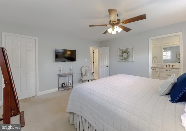 bedroom featuring baseboards, ensuite bathroom, a ceiling fan, and light colored carpet