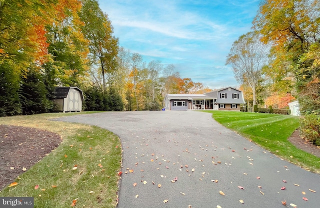 view of front facade featuring a front yard, a storage unit, aphalt driveway, and an outdoor structure