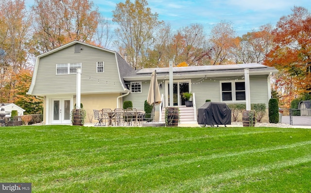 rear view of property featuring french doors, a patio, a lawn, roof mounted solar panels, and fence