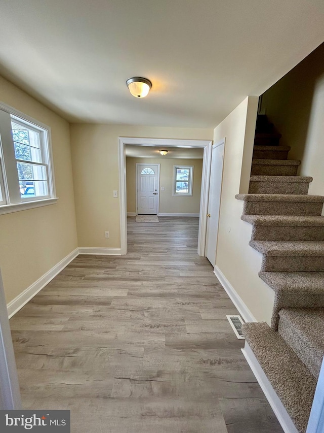 corridor with a wealth of natural light, light wood-type flooring, visible vents, and stairway