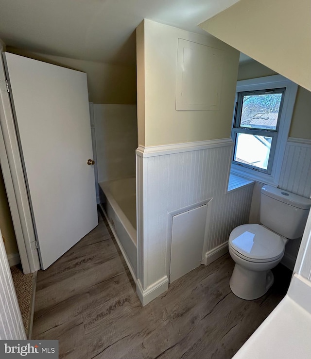 bathroom with a bathing tub, a wainscoted wall, toilet, and wood finished floors