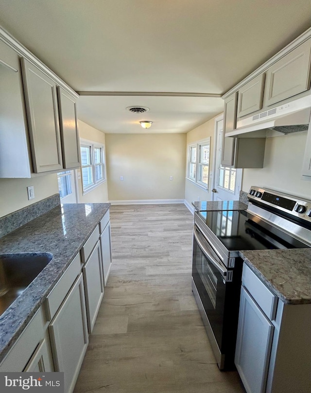 kitchen with stone countertops, under cabinet range hood, visible vents, light wood finished floors, and stainless steel range with electric stovetop