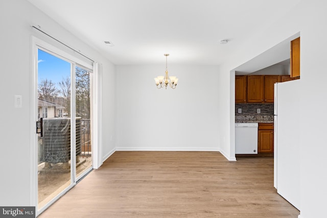 unfurnished dining area with a chandelier, visible vents, light wood-style flooring, and baseboards