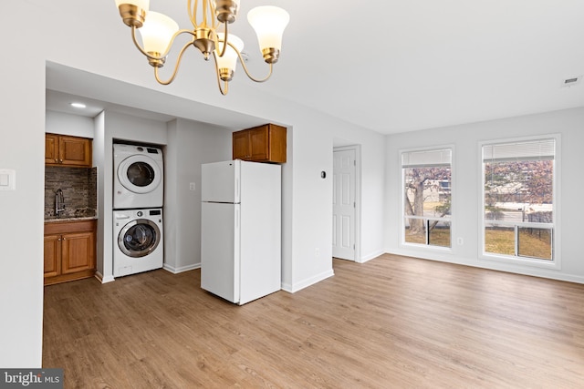 kitchen with freestanding refrigerator, brown cabinets, stacked washing maching and dryer, and an inviting chandelier