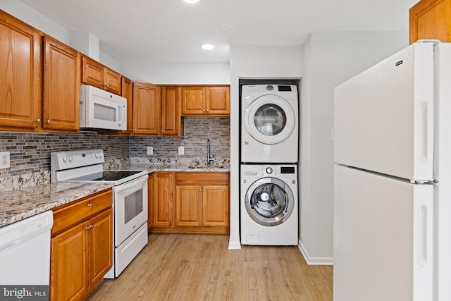 kitchen with white appliances, tasteful backsplash, stacked washer / dryer, light wood-style floors, and a sink