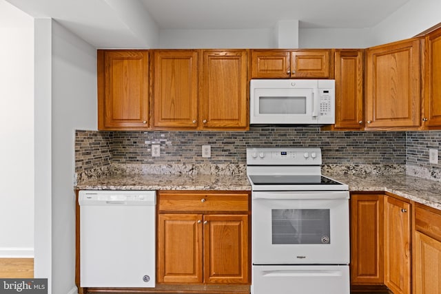 kitchen with white appliances, light stone counters, brown cabinets, and backsplash