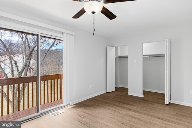 unfurnished bedroom featuring ceiling fan, light wood-style flooring, visible vents, baseboards, and multiple closets