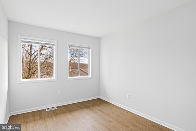 spare room featuring wood finished floors, visible vents, and baseboards