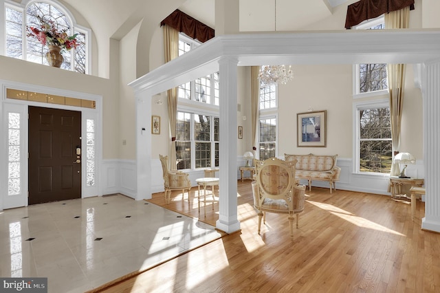 entrance foyer featuring decorative columns, wood finished floors, a towering ceiling, and a chandelier