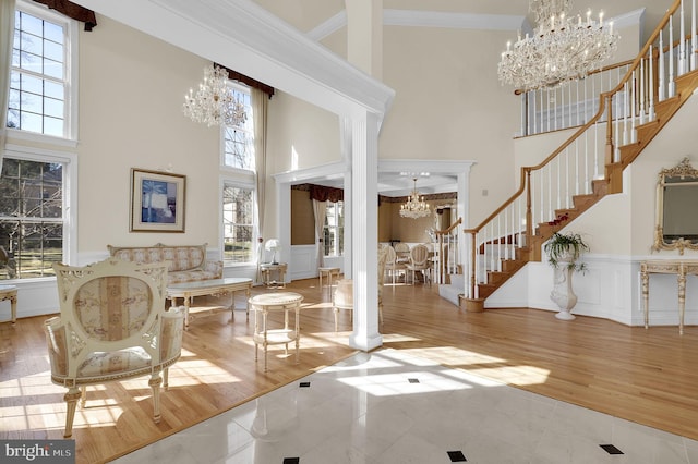 foyer entrance with stairway, wood finished floors, ornamental molding, a towering ceiling, and a chandelier