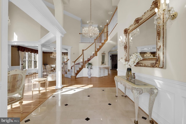 entryway with stairway, wainscoting, a high ceiling, and an inviting chandelier