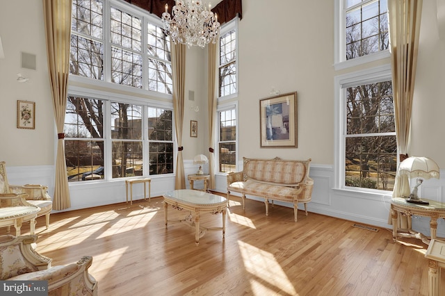 sitting room with visible vents, a chandelier, wainscoting, a towering ceiling, and wood finished floors