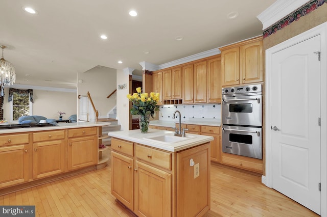 kitchen with a sink, crown molding, light countertops, stainless steel double oven, and a kitchen island with sink