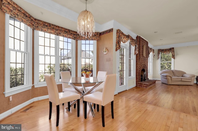 dining room with visible vents, a notable chandelier, light wood-style floors, crown molding, and a fireplace