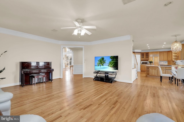 living area featuring crown molding, light wood-style flooring, ceiling fan with notable chandelier, and baseboards