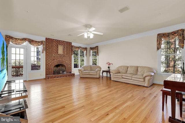 living room with a ceiling fan, crown molding, a fireplace, and light wood finished floors