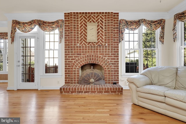 living area with a wealth of natural light, ornamental molding, a fireplace, and wood finished floors