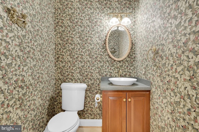 bathroom with vanity, toilet, and wallpapered walls