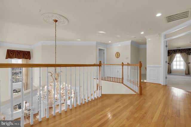 corridor with visible vents, an upstairs landing, hardwood / wood-style floors, crown molding, and a chandelier