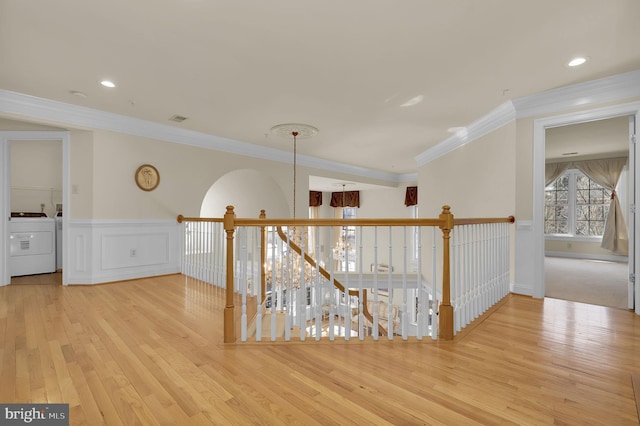 hallway featuring wood finished floors, washer / clothes dryer, wainscoting, crown molding, and a chandelier