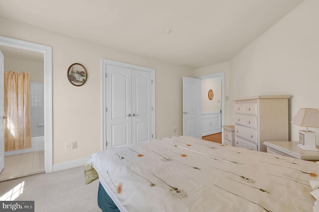 bedroom with baseboards, a closet, ensuite bathroom, and light carpet