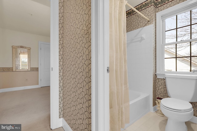 bathroom with wallpapered walls, shower / tub combo, toilet, and wainscoting