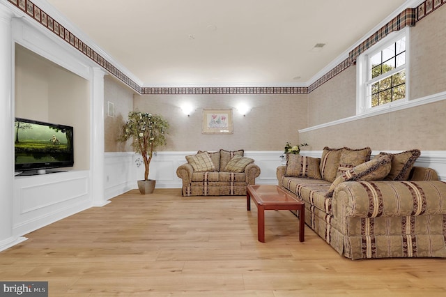 living room with wood finished floors, a wainscoted wall, and ornamental molding