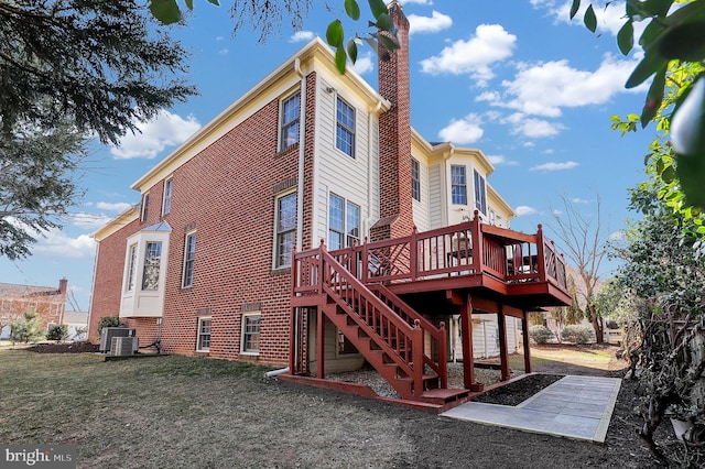 back of house with a wooden deck, a yard, a chimney, central air condition unit, and brick siding