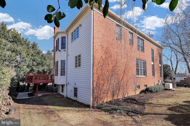 view of side of property featuring a wooden deck, brick siding, and a chimney