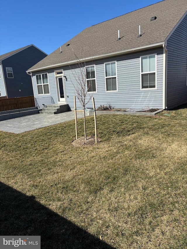 rear view of house featuring roof with shingles, a lawn, and a patio