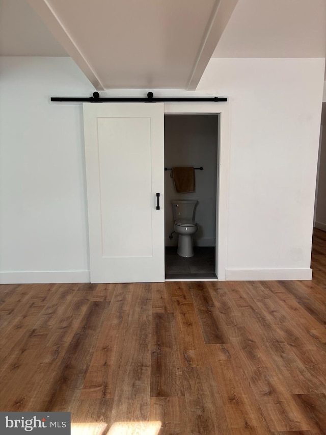 interior space with a barn door, baseboards, wood finished floors, and ensuite bathroom