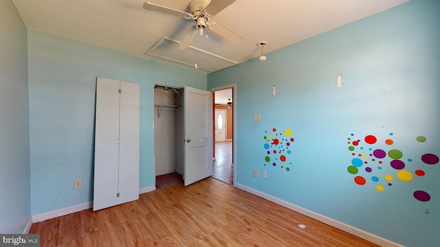 unfurnished bedroom with a closet, wood finished floors, attic access, and baseboards