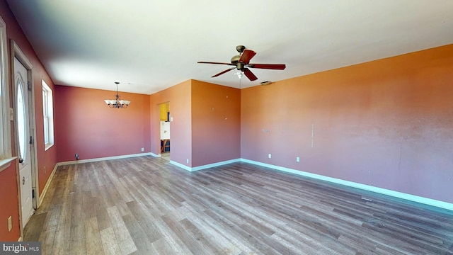 unfurnished room featuring ceiling fan with notable chandelier, light wood-type flooring, and baseboards