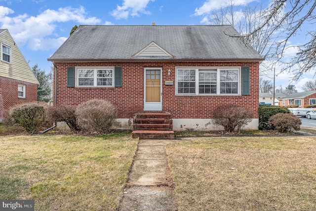 view of front of house featuring a shingled roof, entry steps, brick siding, and a front yard