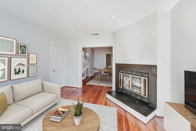 living area featuring baseboards, visible vents, wood finished floors, and a glass covered fireplace