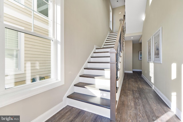 staircase with a high ceiling, wood finished floors, and baseboards