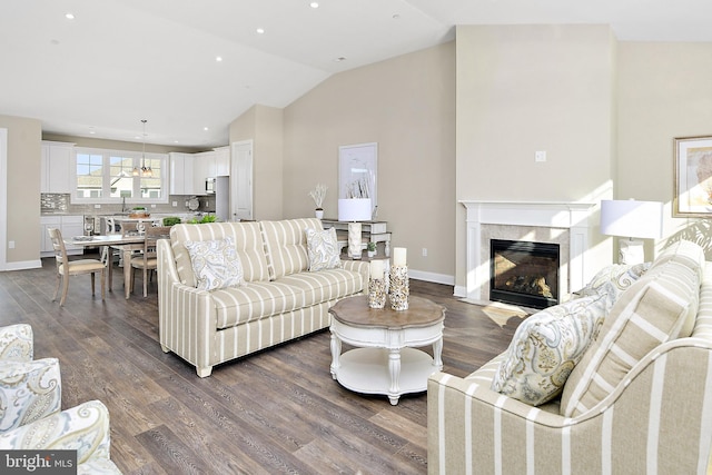 living area featuring dark wood finished floors, recessed lighting, a high end fireplace, vaulted ceiling, and baseboards