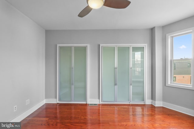 empty room with a ceiling fan, baseboards, visible vents, and wood finished floors