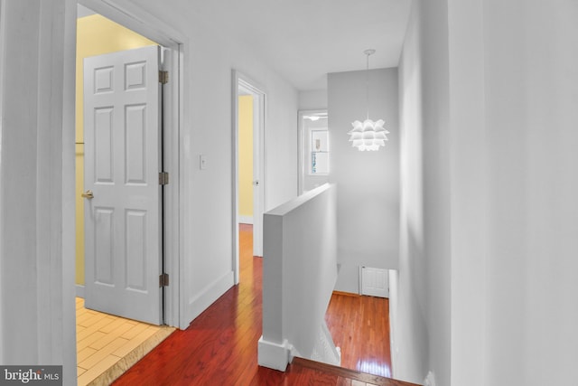 hall featuring wood finished floors, visible vents, baseboards, an upstairs landing, and an inviting chandelier