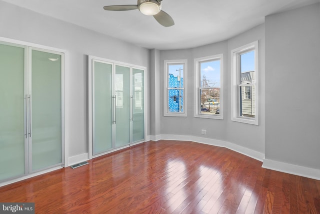 unfurnished bedroom with multiple closets, wood-type flooring, visible vents, ceiling fan, and baseboards